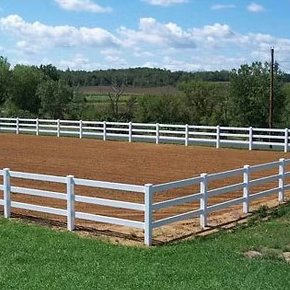 A three rail post surrounding a horse corral.