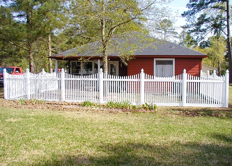 A red house is surrounded by a scalloped picket fence.